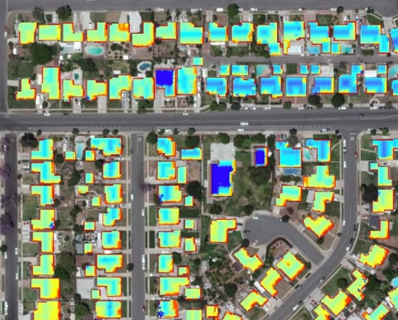 Aerial view of a residential neighborhood with every rooftop shaded from blue to red by modeled annual solar suitability — blue where planes are shaded or poorly oriented, red where sun exposure is highest.